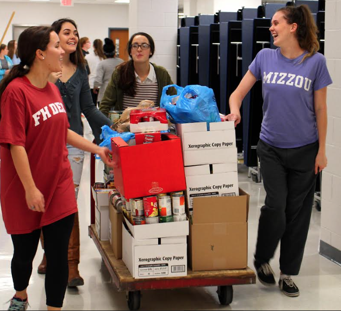 Junior Sammy Markus, Senior Kennedy Cooper, Juniors Celine Jennings and Megan Schulz walk towards the teacher lounge to unload their cart, Nov. 18.  There is about 10 core members who show up to all of the events, Cooper said. Plus the boxes were heavy to unload. The students had walk around to different classroom to collect the boxes of cans.