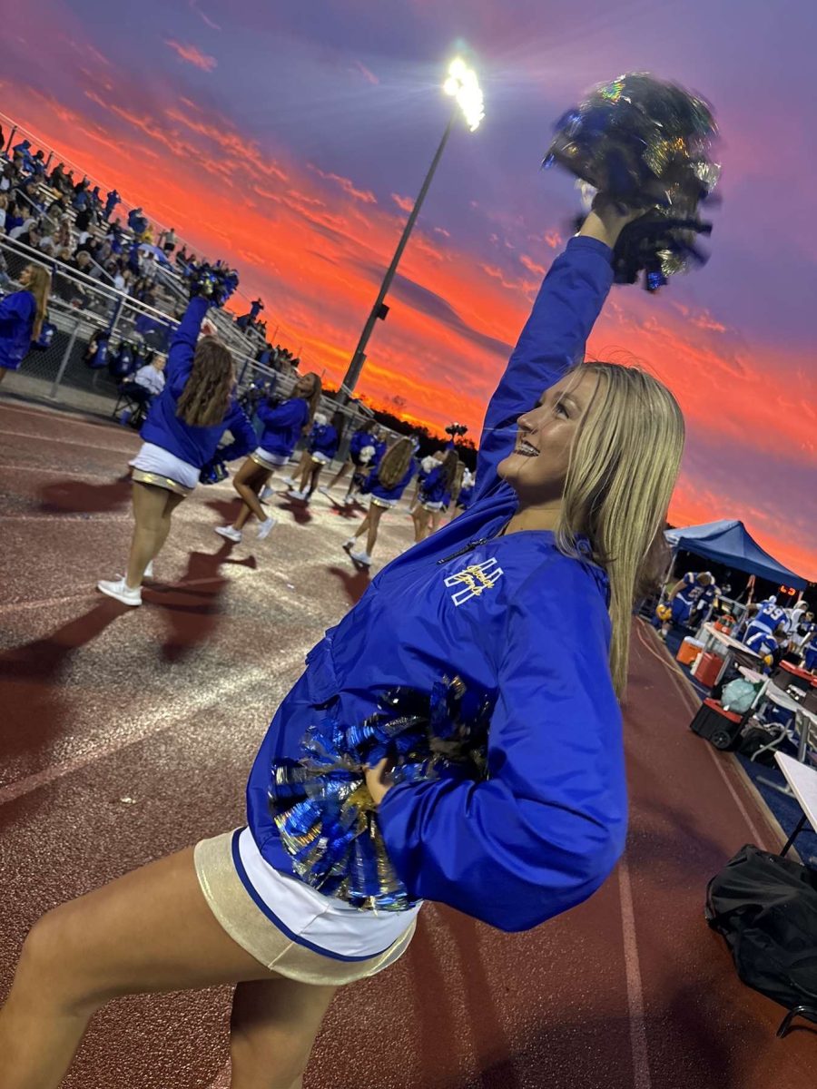 Sunset Spirit – Junior Taylor Ricketson raises her pom-poms as she cheers at a football game under the sunset. Earlier that evening, the team had gathered to excite each other for their halftime performance. “The energy from the crowd always makes these games unforgettable,” Ricketson said.